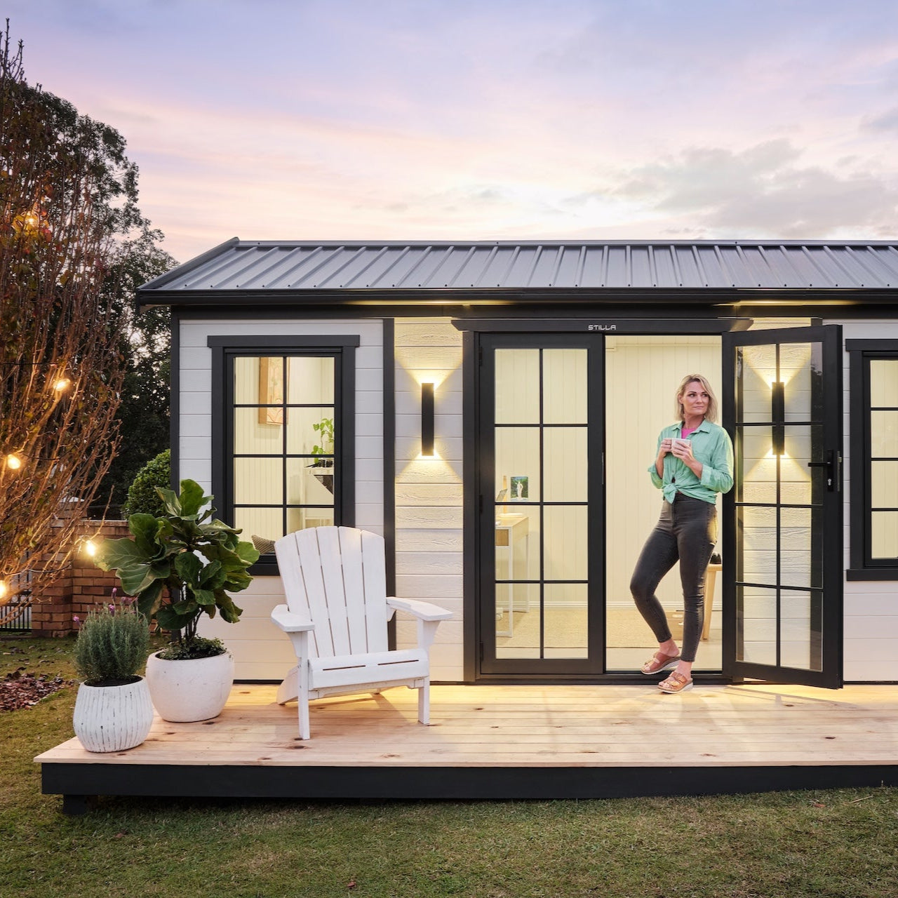 Modern shed with a person standing inside, surrounded by plants and outdoor furniture.